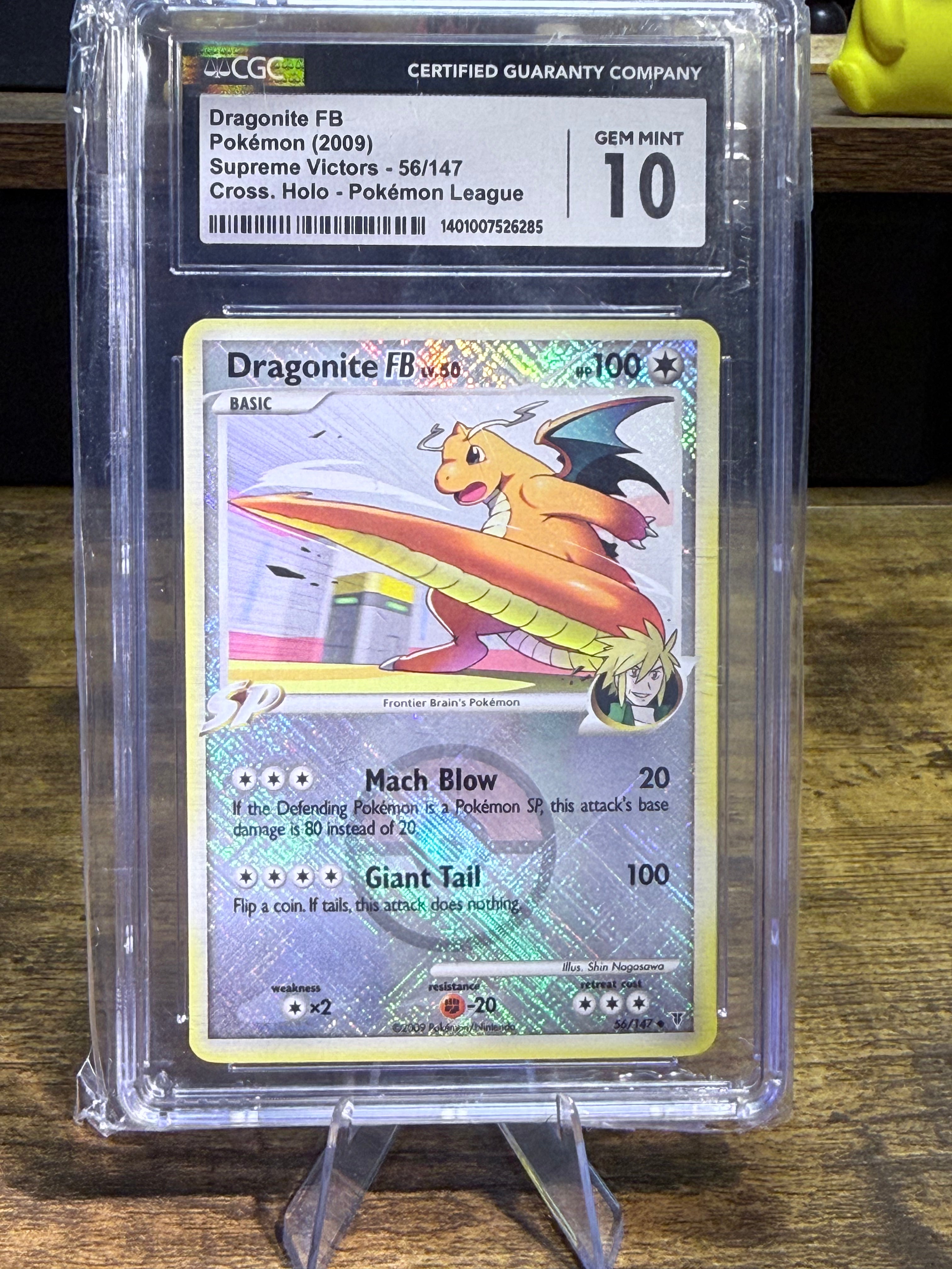A graded Pokémon Dragonite trading card inside a clear plastic protective slab, with the grading label visible at the top. The card is photographed standing on a small clear display stand on a wooden surface.