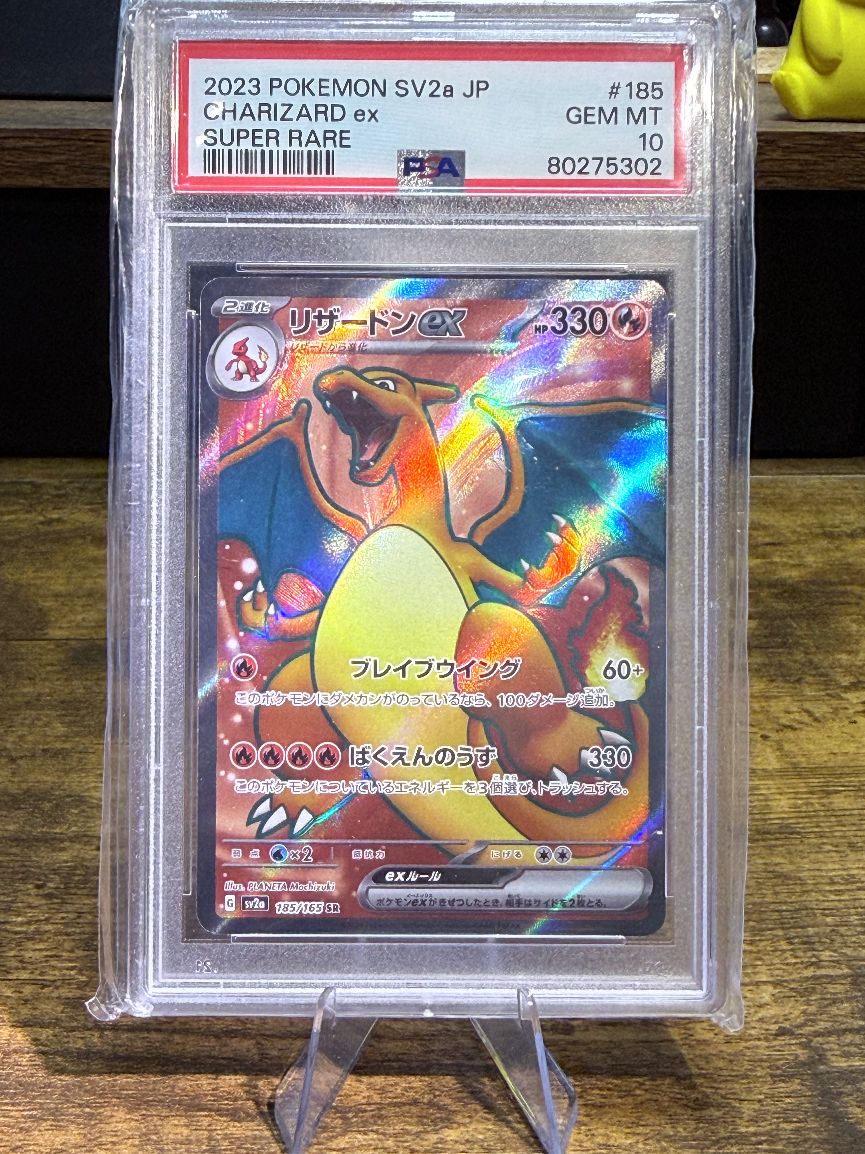 A graded Pokémon Charizard SV2 2a JP trading card inside a clear PSA Gem Mint protective case, displayed on a stand over a wooden surface.