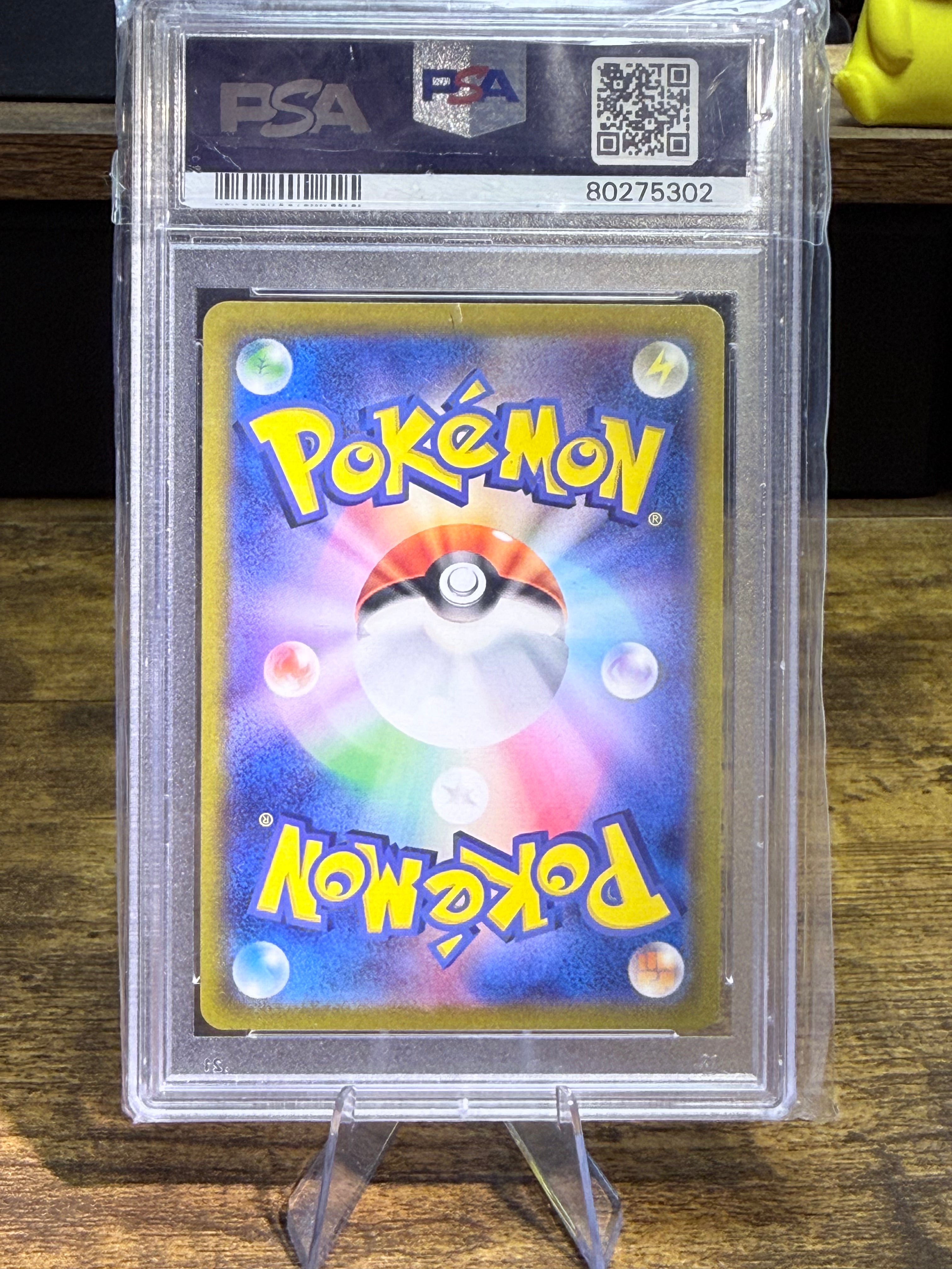 A graded Pokémon trading card inside a clear PSA slab, displayed on a small stand on a wooden surface.